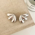 Macro detail of silver wing-shaped stud earrings on rustic linen with a candle background - Silver