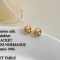 Close-up of elegant gold oval stud earrings with polished mirror finish on a ceramic plate - Gold Earrings