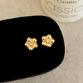 Detail of gold flower earrings with wavy petals and a crystal center on a black stand - Gold
