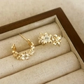 Detailed close-up of golden floral earrings with white enamel and sparkling zircon - White