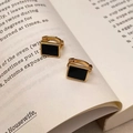 Dettaglio di orecchini rettangolari in smalto nero e oro su una pagina di un libro - Chiusura a Cerchio Dorata con Piastra Nera