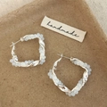 Detail van gedraaide kristallen oorringen met zilveren basis op een handgemaakt label - Witte kristallen oorbellen