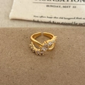Nahaufnahme des goldenen Crossover-Rings mit Zirkonia-Steinen auf strukturiertem Papier - Gold