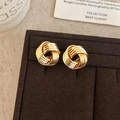 Detail of gold twisted knot stud earrings on a brown velvet jewelry display stand - Gold