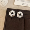 Detailed close-up of silver braided knot stud earrings on dark velvet display - Silver
