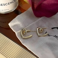 Close-up of golden hollow twisted heart earrings on white silk pouch with petals - Gold
