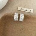 Détail macro de boucles d'oreilles créoles rectangulaires texturées sur boîte vintage - Boucles d'Oreilles Clous Rectangulaires Argentées Texture Lave / Argenté
