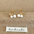 Detalle de pendientes de mariposa dorada con perlas sobre fondo rústico de papel marrón - Dorado