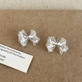 Boucles d'oreilles nœuds argentées avec zircons étincelants sur fond brun - Boucles d'Oreilles Clous Noeud / Argenté