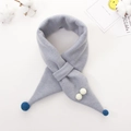 Dettaglio della maglia di una sciarpa calda per bambini con pompon bianchi e chiusura a incrocio - Celeste