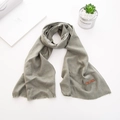 Dettaglio sciarpa in maglia verde oliva con frange e toppa in pelle su sfondo bianco - Verde mela