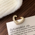 Dettaglio di un ear cuff a cuore dorato con zirconi micro-pave su uno sfondo estetico - Polsino per Orecchie Cuore Oro