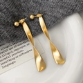 Detailweergave van lange gedraaide matgouden oorbellen op een minimalistisch oppervlak - Lange Oorknopjes / Goud