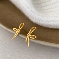 Macro detail of gold bow knot earrings resting on a dark ceramic dish with a soft background - Gold