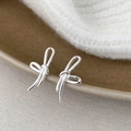 Detailed close-up of silver bow-shaped stud earrings on a brown ceramic plate - Silver