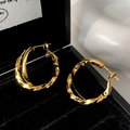 Detailansicht verschlungener goldener Creolen mit glatter und gedrehter Textur-Optik - Goldener Kreuzreifen / Gold