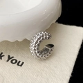 Dettaglio macro di un earcuff a C argento con texture a perline su cartoncino beige - Argento