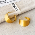 Dettaglio macro di orecchini a C in oro opaco spazzolato su sfondo di tela beige - Oro