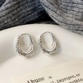 Dettaglio di orecchini a cerchio intrecciati argento su vassoio in ceramica elegante - Argento