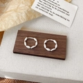 Macro shot of silver metal hoop earrings with a segmented design on a rustic wooden stand - Silver