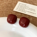 Close-up of burgundy square enamel stud earrings with a glossy finish on a white plate - Ancorra Red