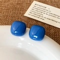 Detail of dark blue glossy square stud earrings placed on a white ceramic plate - Light Blue