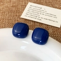 Close-up of deep blue resin square stud earrings with high-gloss finish on a ceramic plate - Dark Blue