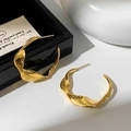Nahaufnahme goldener Blattohrringe mit gedrehten Metallfalten und glänzendem Finish - Gold