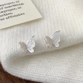 Detailansicht der silbernen Schmetterling-Ohrstecker mit matter Oberfläche auf Strickware - Silber