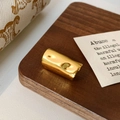 Dettaglio del copriorecchio dorato con texture irregolare su legno scuro - Oro