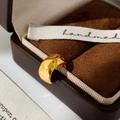Detail van een vergulde ear cuff met onregelmatige gehamerde textuur op een fluwelen doos - Goud