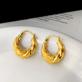 Dettaglio di orecchini a spirale dorati con trama intrecciata su un piatto bianco - Oro