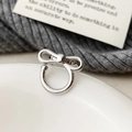 Dettaglio macro di un ear cuff a fiocco in argento minimalista su un piatto di ceramica - Argento