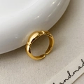 Detail van verstelbare gouden ring met ribbeltextuur op wit keramiek en linnen stof - Goud