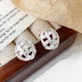 Detalle de pendientes de bola tejida plateada sobre un joyero de madera con fondo decorativo - Plateado
