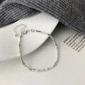 Detail eines silbernen Perlenarmbandes mit Karabinerverschluss auf einem weißen Keramiktablett - Facettiertes Perlenarmband