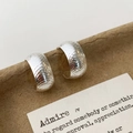 Close-up of silver C-shaped earrings with textured cross-pattern on a brown tray - Cross-Hatched Textured C-Shaped Style (A-1816)