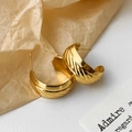 Elegantes pendientes dorados en forma de C con textura cruzada sobre fondo de papel vintage - Dorado