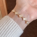 Elegantes vergoldetes Armband mit fünf weißen Kleeblatt-Anhängern am Handgelenk - Gold