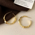 Détail de boucles d'oreilles créoles dorées texture lave sur un fond de tissu doux - Doré