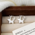 Detailopname van mat stervormige oorbellen met geborsteld zilver op beige stof - Zilver geborstelde ster oorknopjes