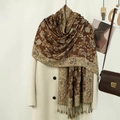 Close-up of retro paisley embroidery on a brown fringed shawl worn over a white coat - Brown
