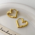 Detail van minimalistische hartvormige oorringen in gouden afwerking op een keramisch bord - Goud