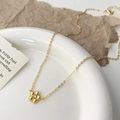 Dettaglio di una delicata collana con pendente a fiore dorato e zircone su un piatto bianco - Collana a Fiore d'Oro