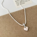 Primer plano del collar corazón de plata con nácar sobre soporte de papel kraft - Collar de Corazón Esmalte Blanco Concha Rosa
