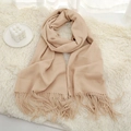 Detail view of a thick beige tassel scarf with soft cashmere-like texture on a white rug - Light Camel