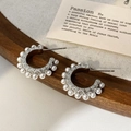 Detailopname van zilveren C-vormige oorbellen met witte parels op een houten achtergrond - Zilver