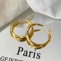 Macro-opname van gouden gedraaide creolen met spiegeling op witte stoffen achtergrond - Glanzende Gouden Creolen