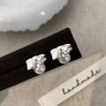 Detalle de pendientes de lazo plateado con perlas en un soporte con textura - Plateado