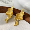 Détail macro de boucles d'oreilles dorées à texture métallique liquide irrégulière sur fond - Doré